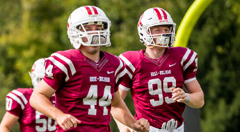 !Image shows two football players in uniform running onto the field for a game. 