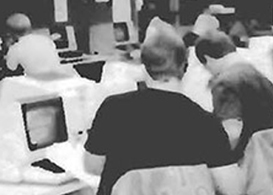 Two students working on a computer in a large computer room with rows of computers on desks.