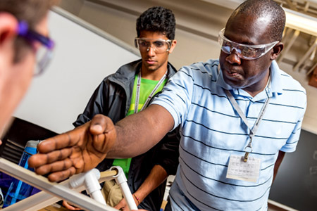 Professor John Aidoo helps students constructing a model of a bridge.