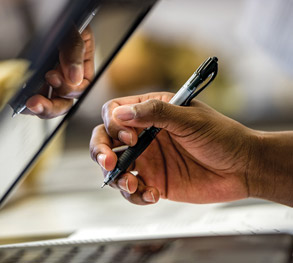 Picture of a hand holding a pen next to a laptop.