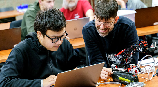 !Computer Science faculty and male students working in a computer class.