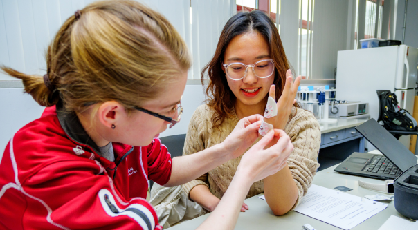 Three biomedical engineering students holding a model of a human leg they designed for the training of medical professionals. 