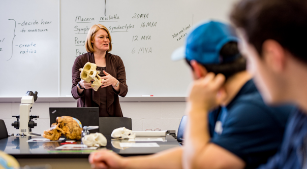 A professor lectures in a biology lab as students listen.