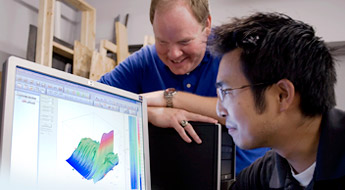 Student getting help from a professor as he examines a 3D diagram on a computer screen.