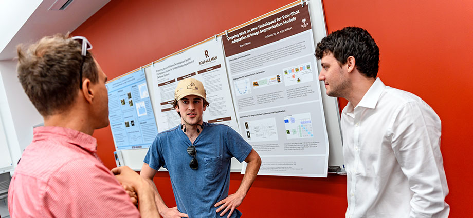Rose-Hulman students stand in front of a poster board presentation.