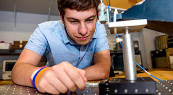 Male student looks closely at electrical device in lab.