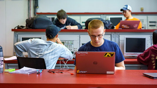 Male professor reaches toward electrical device as female student looks on.