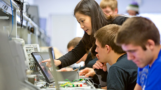 Female professor points to laptop computer screen as male student observes.