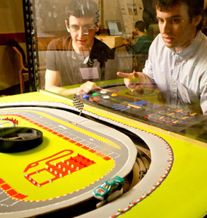 Two male students watch discuss robotic device they created.