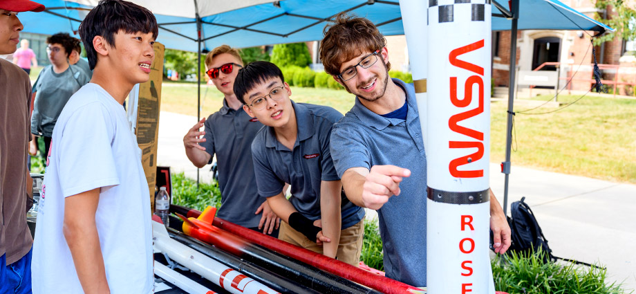 Rose-Hulman students at Welcome Back Wednesday event with rocketry club rockets and NASA sign in background.