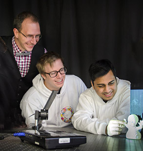 Dr. Kirkpatrick works with two male students in optics lab.