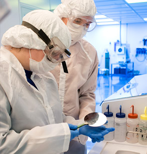 Students in clean room attire examine a metal disc