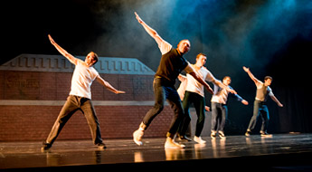 Two male students and one female student in costumes perform on stage.