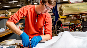 A male student cut a sample of fiber for a composite materials research project.