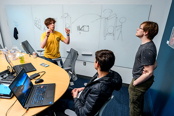 Three students discuss a diagram on a white board in a FAB meeting room.