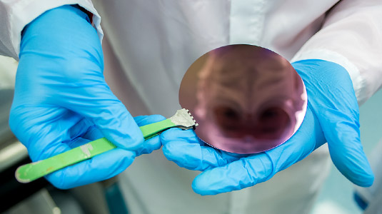 Two gloved hands using an instrument to hold a metal disc.