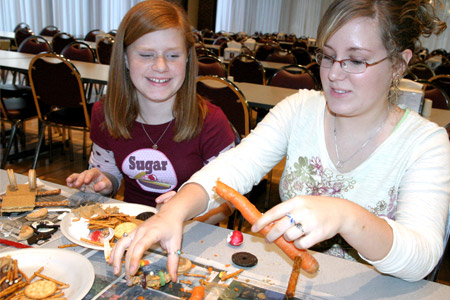 Rose-Hulman student helps smiling younger student build using a carrot, pretzels, and other items during Explore Engineering edible engineering project