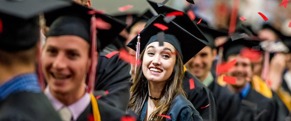 Image shows graduates dressed in their black commencement gowns smiling and walking to their graduation ceremony.