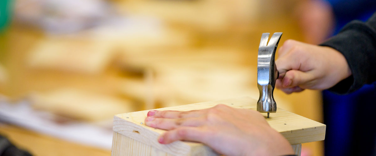 Image shows child's hand hammering a nail into a board. 