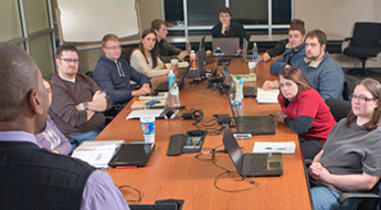 !large group of students sit around table with their laptops