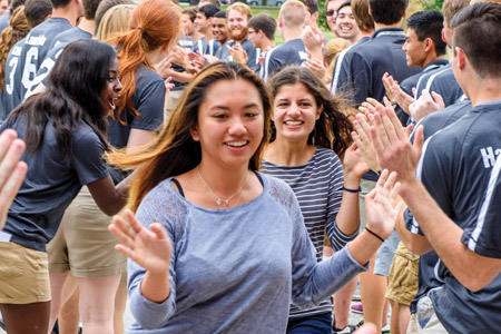 A male freshman student smiles and receives high fives from current residence life counselors during orientation.