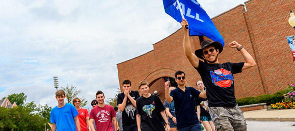 An SA pumps his fist and waves a blue Blumberg Hall flag as he leads his residents up the hill after freshman convocation.