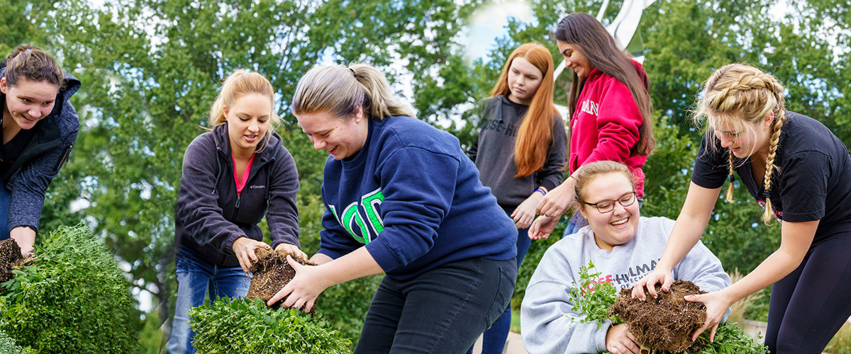 A female student volunteer using a rake to help clean up a property in the community as part of a day of service.