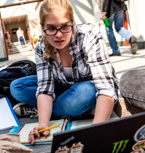 Female student working on laptop while sitting on floor.