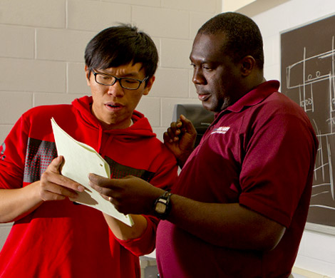 Dr. John Aidoo looks at paper with a student. 