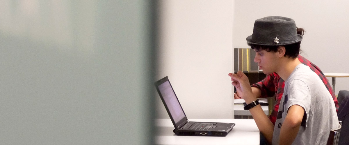 Male student in a hat looking at a laptop computer.