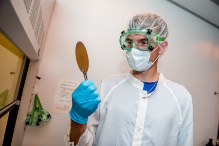 Student in clean room wearing a mask and looking at something he is working on.