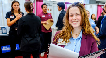 A smiling student in professional clothing holds a portfolio and resume at the Career Fair.