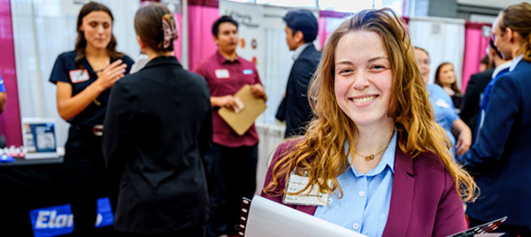 A smiling student in business clothes holds a resume and portfolio at the Career Fair.