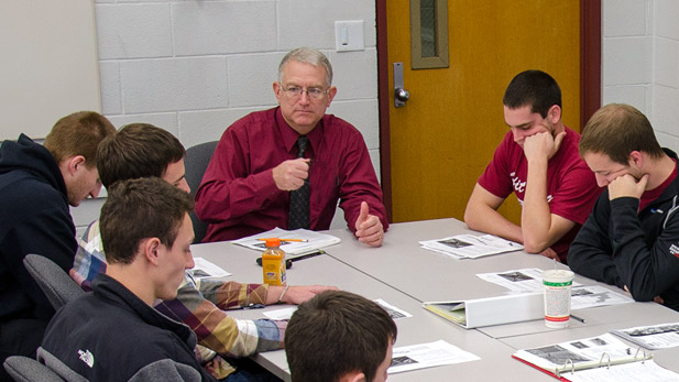 Professor Kevin Sutterer sitting a table talking with students