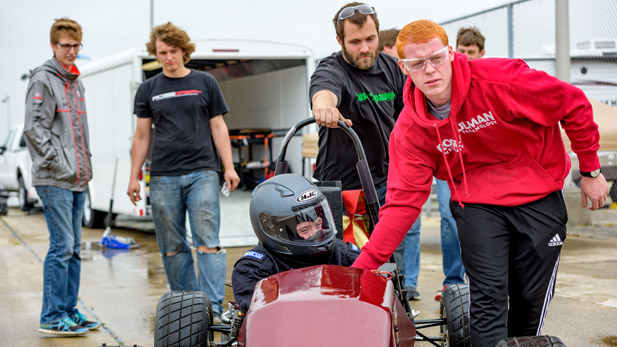 Students running alongside their Formula SAE racecar during a practice run