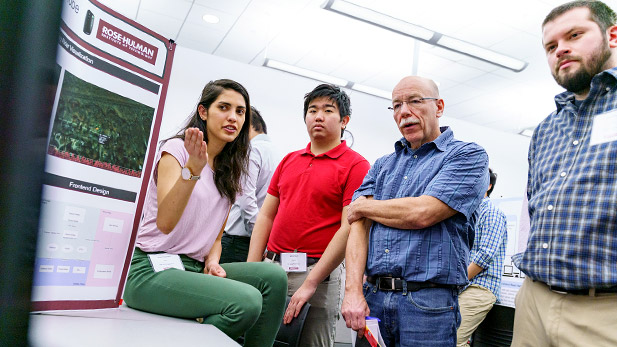 A student gesturing to her project's display board at the CSSE senior expo