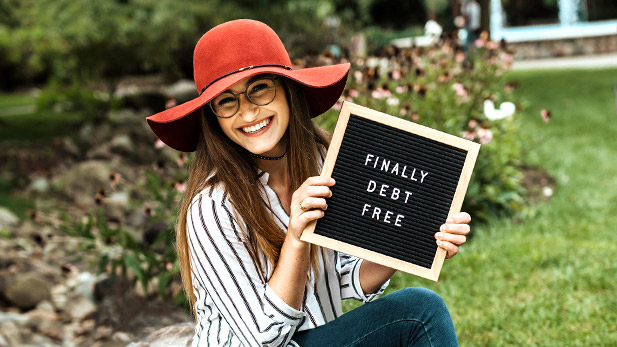 Image shows Madison Murphy smiling and holding a sign reading "Finally Debt Free." 