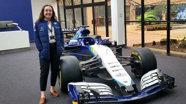 Gabbie Gilbertson stands smiling next to a race car