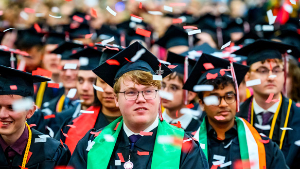 Graduates celebrate as red and white confetti falls.