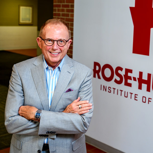 Rose-Hulman President Robert A. Coons poses in front of Rose-Hulman logo wall.