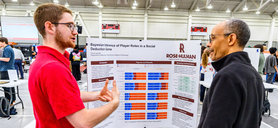 Daniel Leverett presents his research on a trifold board to a professor.