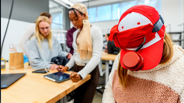 Biomedical engineering students demonstrate their device, which clips onto the brim of a baseball cap.