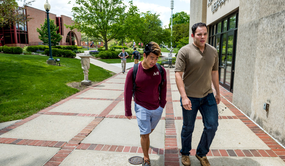 Two male students walking outside of the Logan Library. 